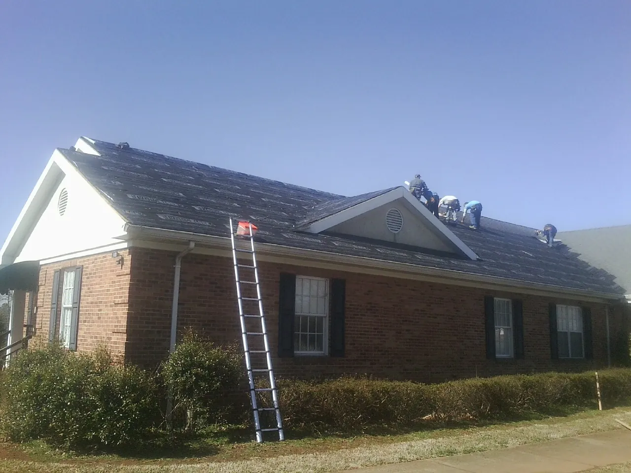 Crew tearing shingles off a brick ranch roof with a ladder set — Emergency Roof Repair work by our crew in Albright