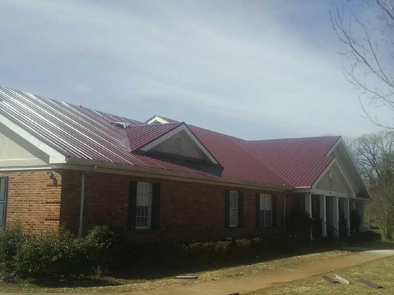 Red metal roof with gabled entries on a long brick building, from a Hail Damage Roof Repair job in Albright