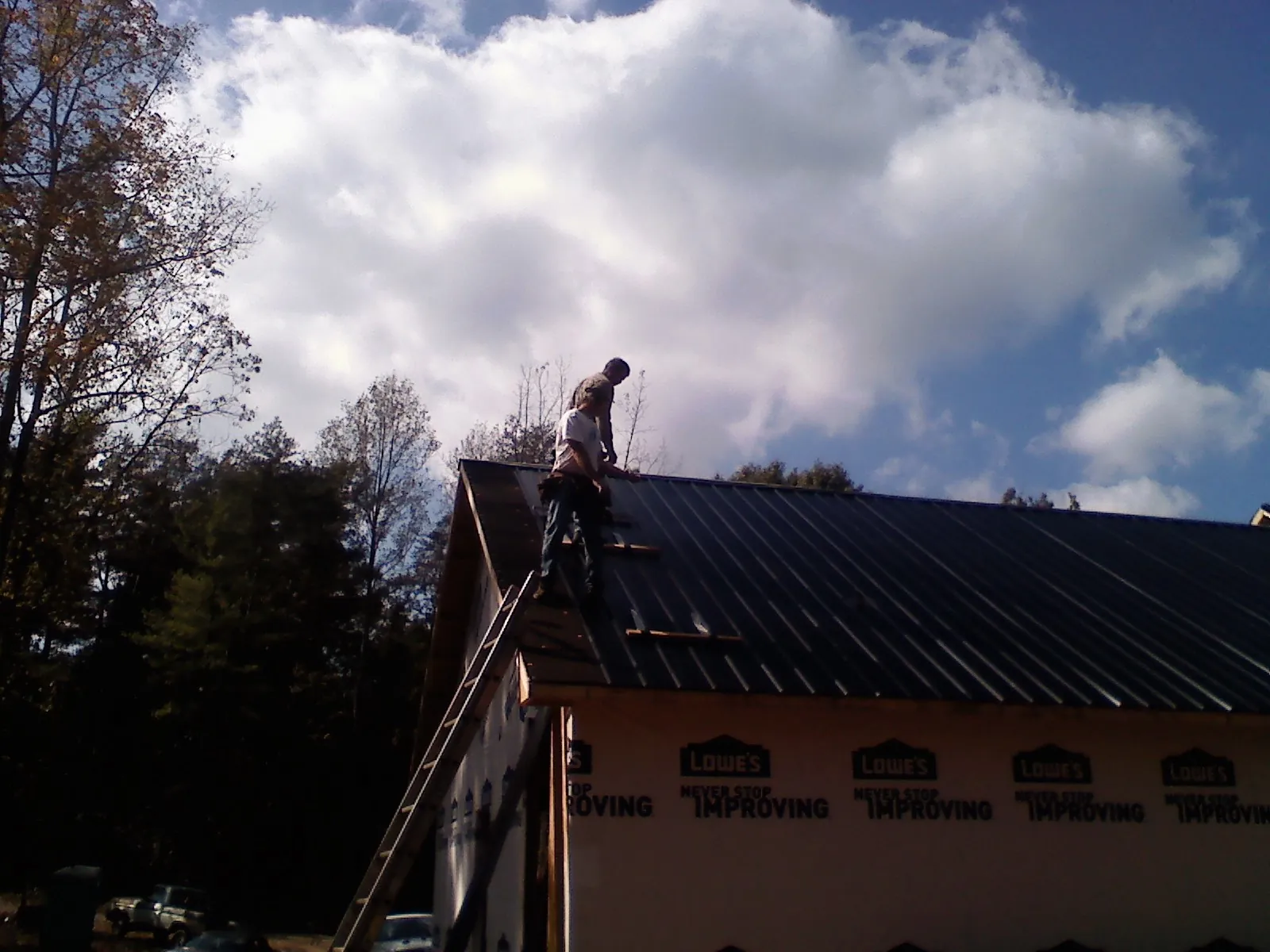 Roofer fastening dark metal panels high against a cloudy sky, from a Roof Inspection job in Albright