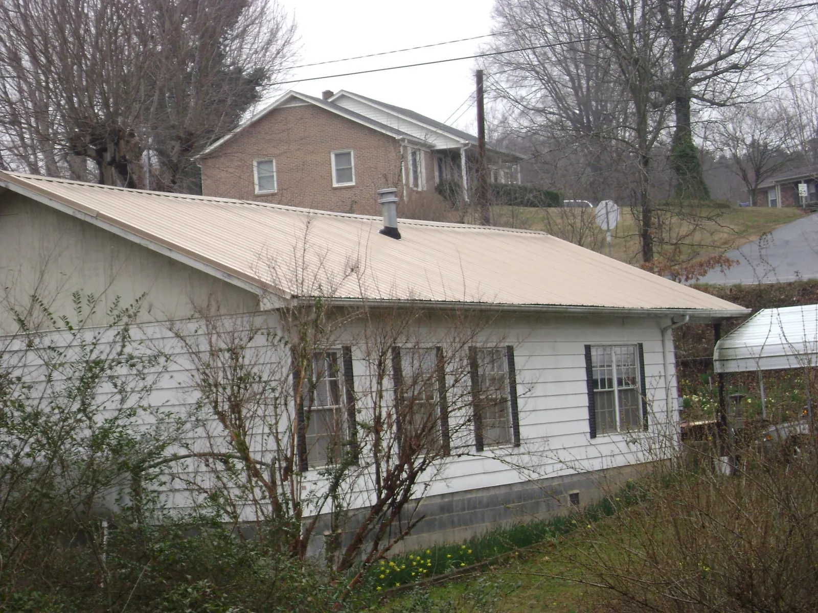Tan metal roof on a white sided house set into a hillside — Commercial Roofing by Roofing Brothers in Albright